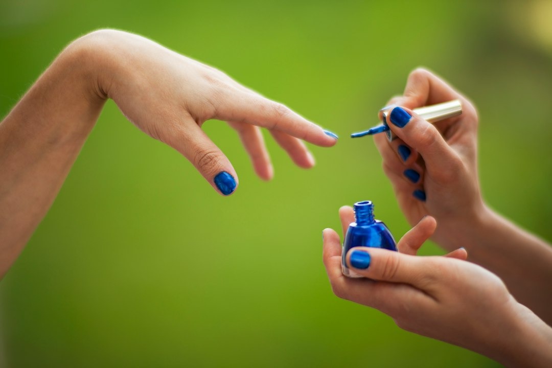 Hands applying blue nail polish to fingernails.